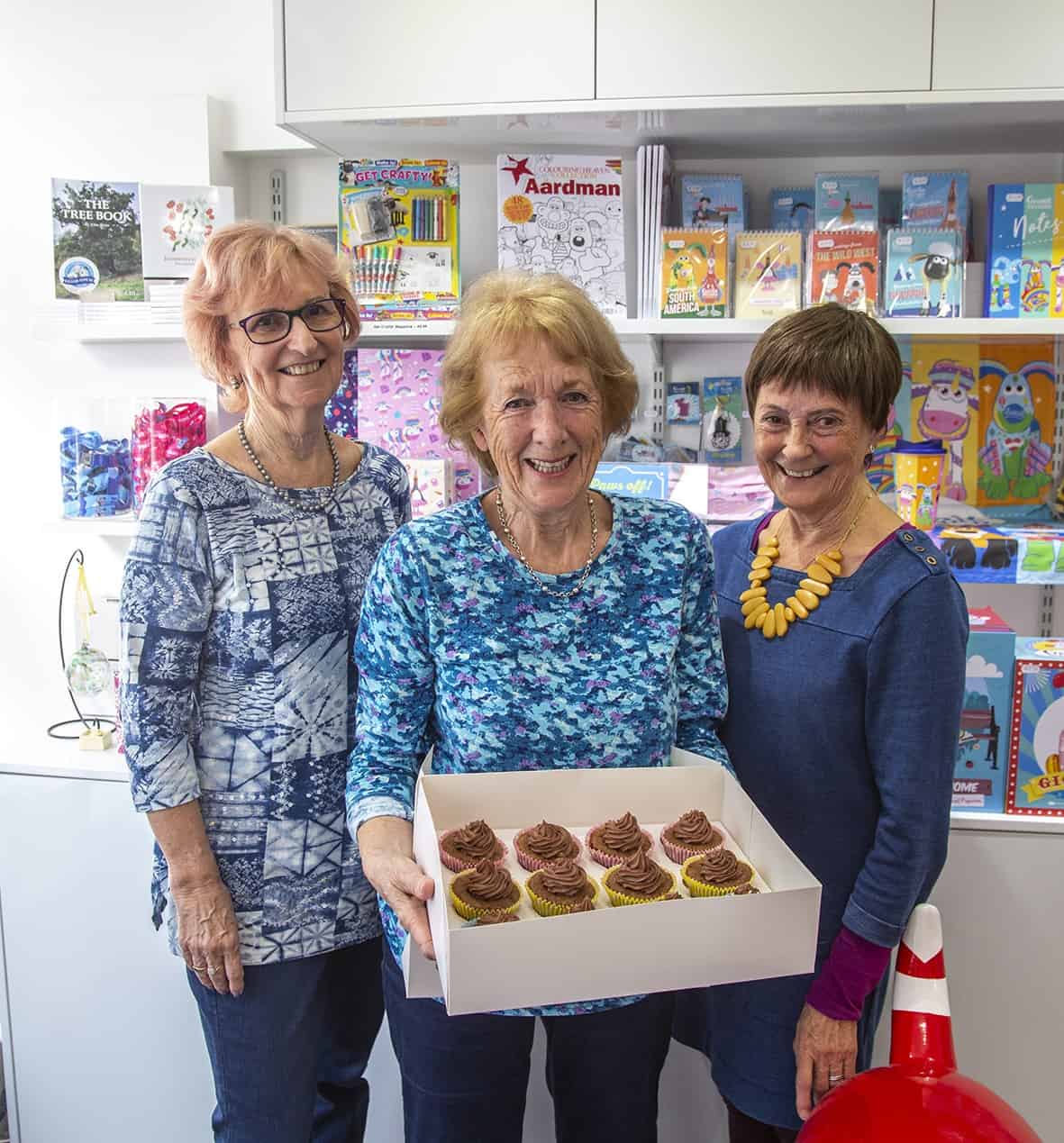 Three women holding a tray of cakes