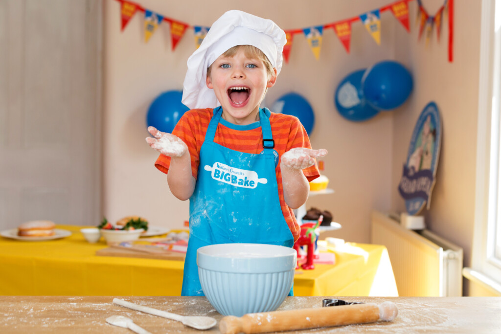 A child baking with a 'big bake' apron and bakers hat on. 
