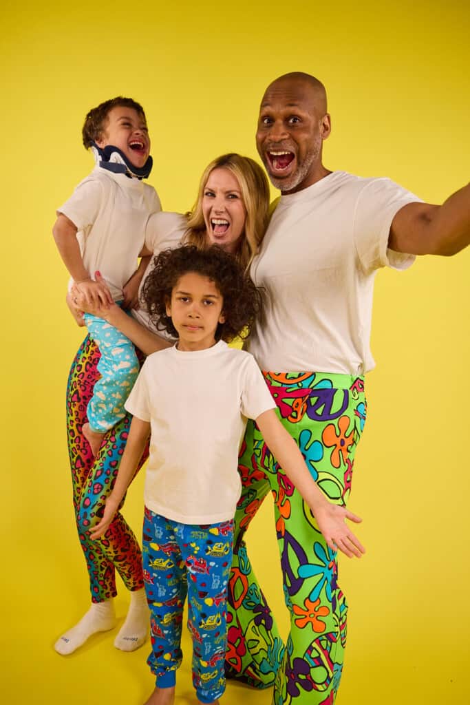 Family wearing white t-shirts, wrong trousers and yellow background. Family getting involved with Bristol charity fundraising event where they are wearing their funky trousers to raise money for sick kids. The photo is showing families can get involved in Wallace & Gromit's Wrong Trousers Day.