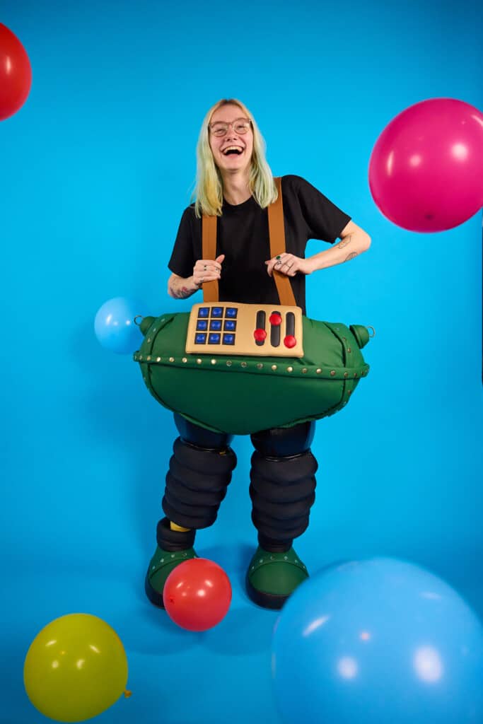 Girl joins in wrong trousers day event by wearing her funky flares and legwear to raise money for Bristol Children's Hospital. She wears a blakc top, Wallace & Gromit's techno trousers and the background is blue. The photo is showing people can get involved in Wallace & Gromit's Wrong Trousers Day at home or from work.