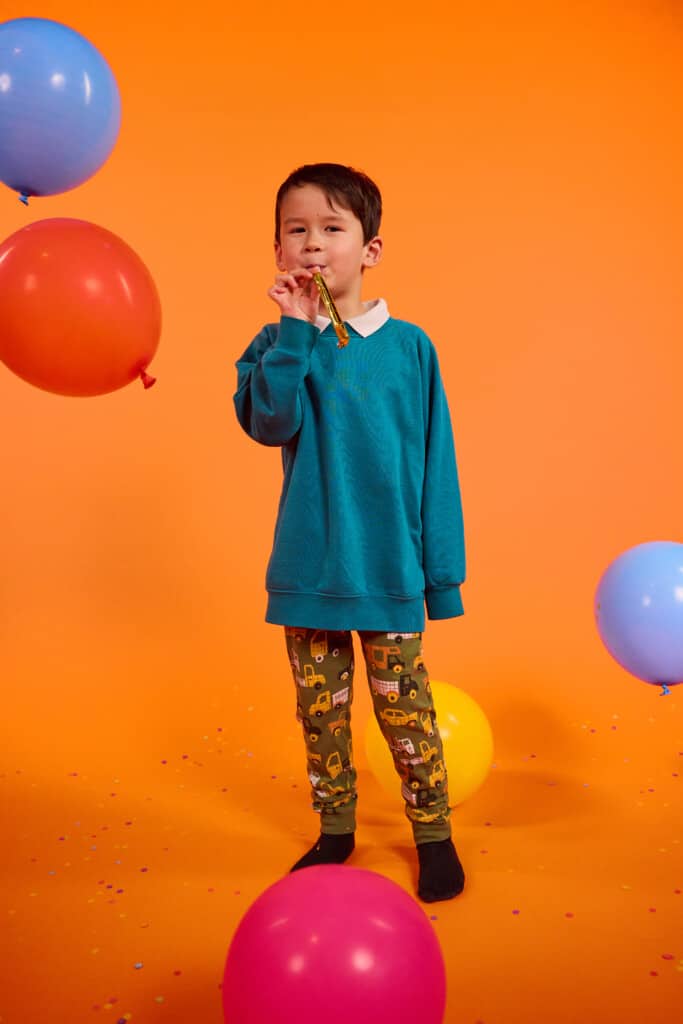 A young small school boy participating in annual fundraising event the Wrong Trousers Day. School kids and schools taking part in the non-uniform day. Young school child wearing blue jumper, wrong trousers with an orange background. The photo is showing schools and nurseries can get involved in Wallace & Gromit's Wrong Trousers Day.