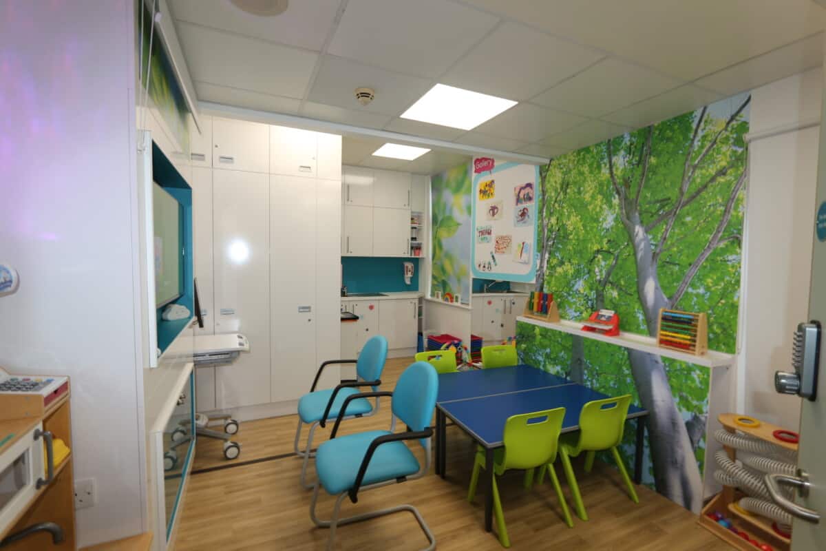 The Caterpillar Ward play room, with toys, a table and chairs, a television and a small kitchen.