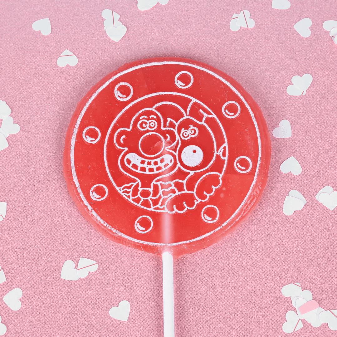 A pink candy lollipop with Wallace & Gromit engraved. Placed on a pink backround surrounded by white love heart confetti.