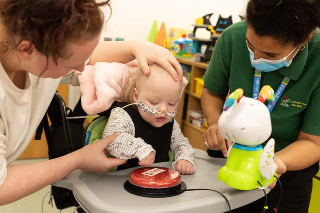 A little girl with two tubes in her nose plays with sensory toys in Bristol Children's Hospital alongside her mum and a Play Assistant.