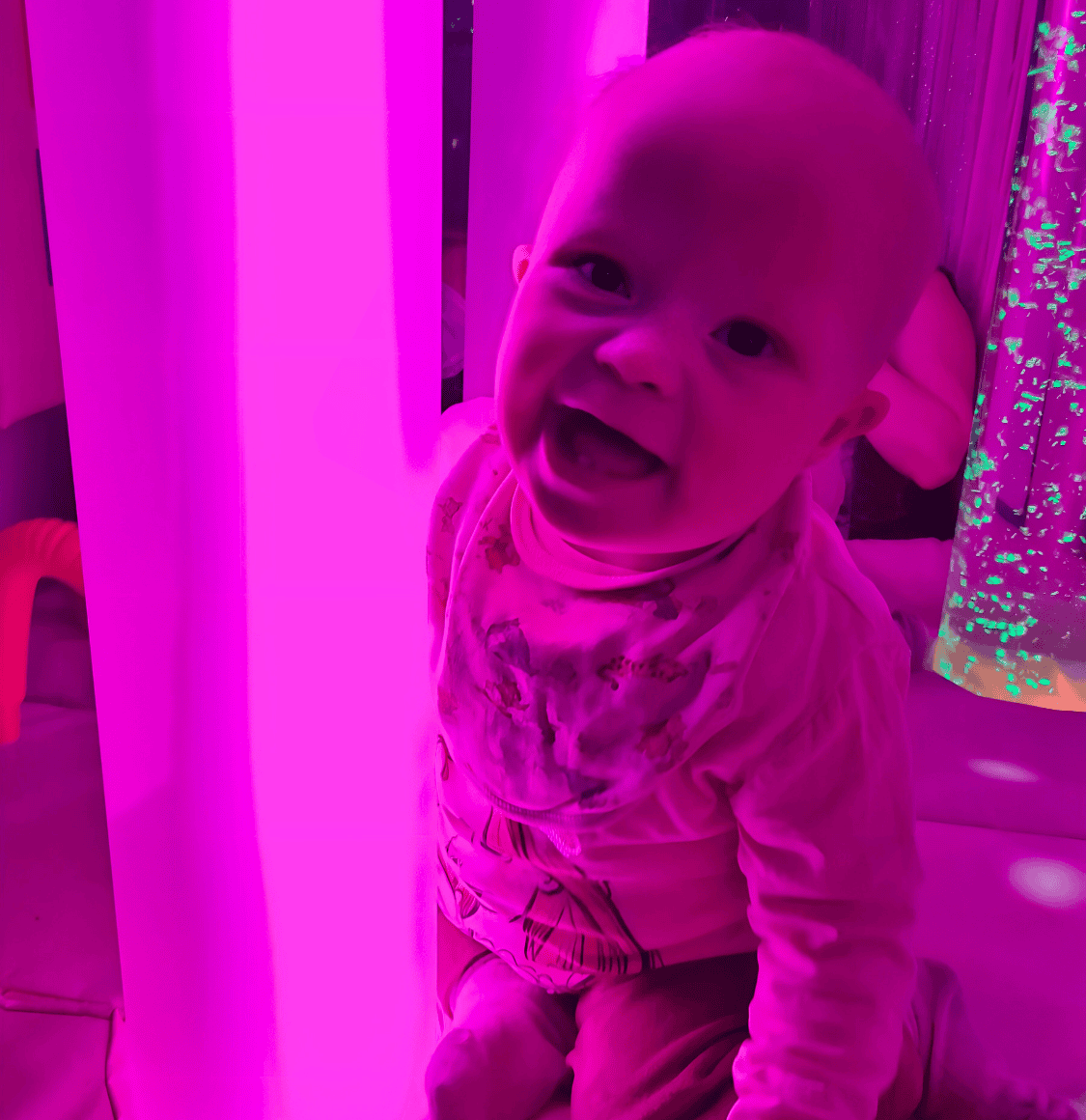 A young child hugging a cylindrical light tube, smiling at the camera