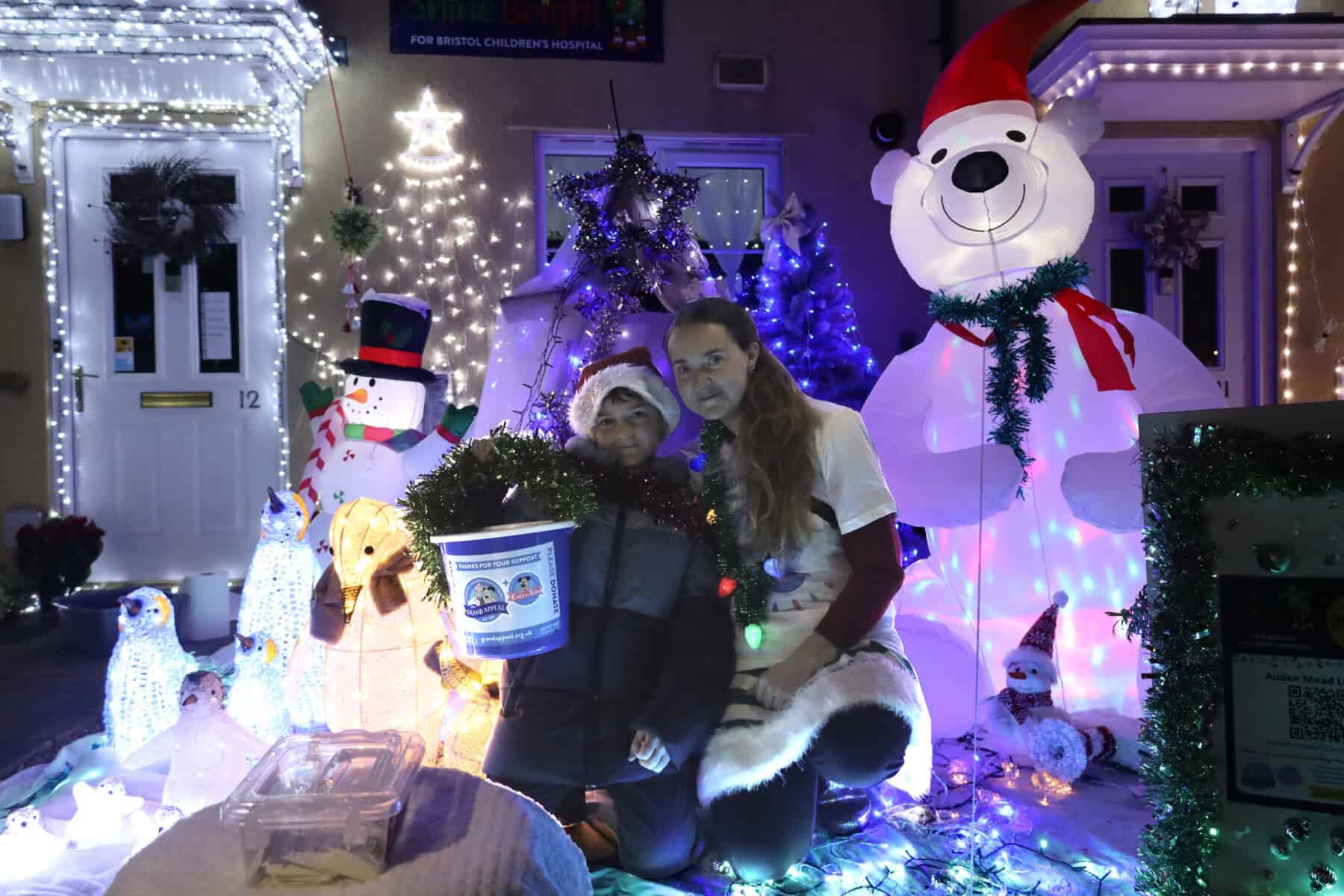 Kelly and Cameron are stood in front of a bright Christmas display, holding a donation bucket