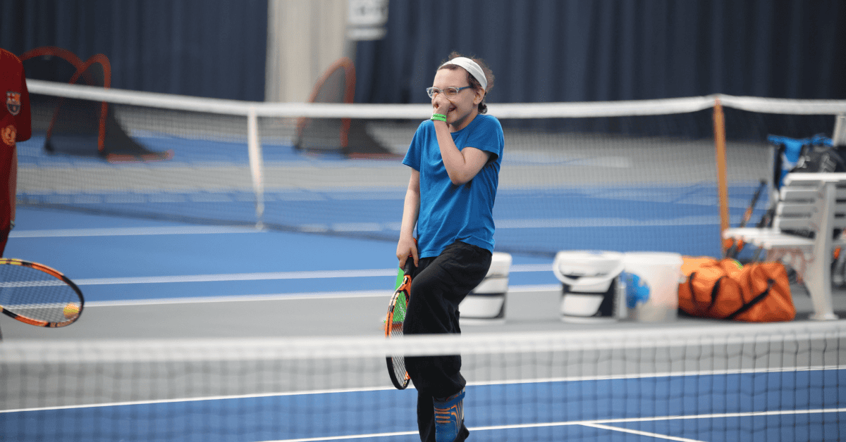 A girl on a tennis court at 'Make a Move!', laughing.